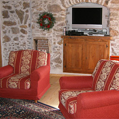 Wnetrze pokoju dziennego w stylu rustykalnym z dwoma fotelami z czerwoną, wypraną tapicerką i czarno-bordowym wyczyszczonym dywanem.